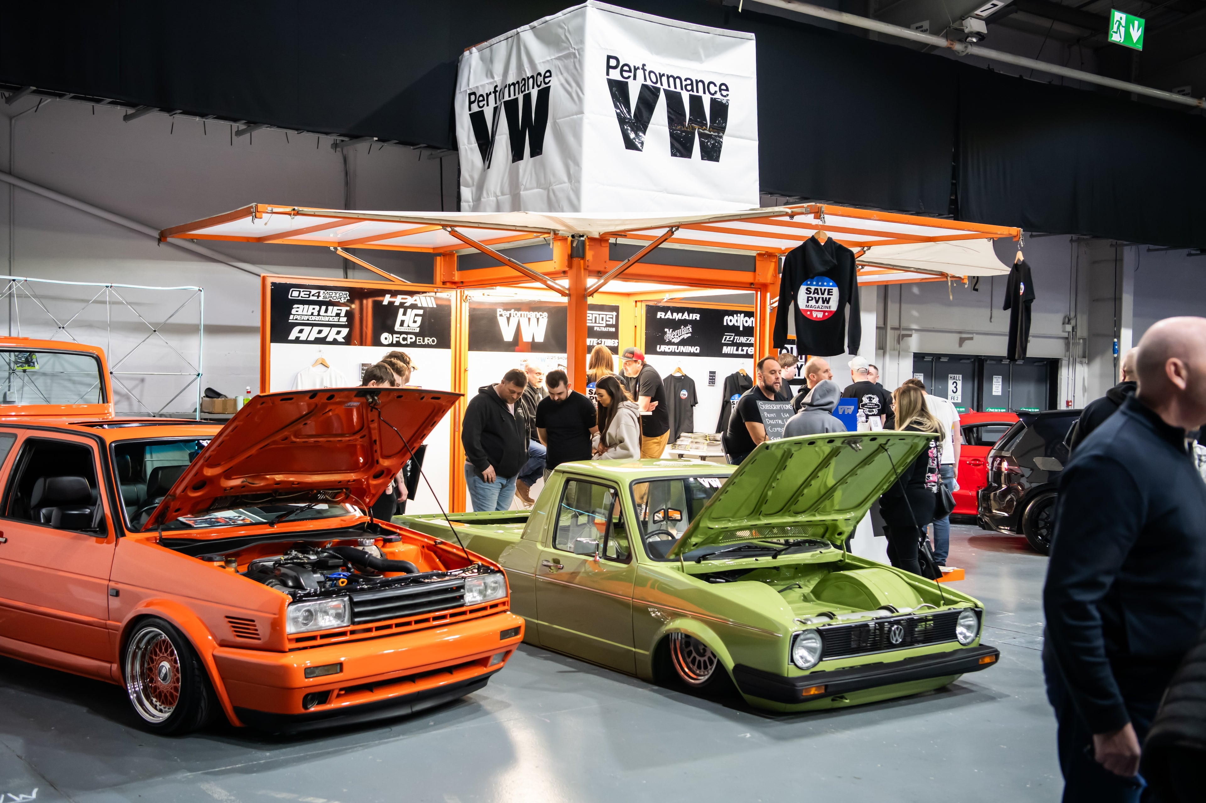 Two modified cars on display at a car show with 'Performance VW' branding.